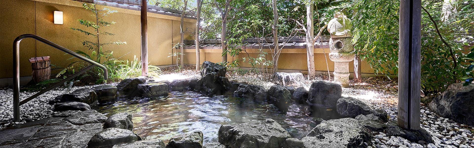 Yamatoya Besso Water surrounded by stacked dark boulders, deciduous trees, and pale stone walls
