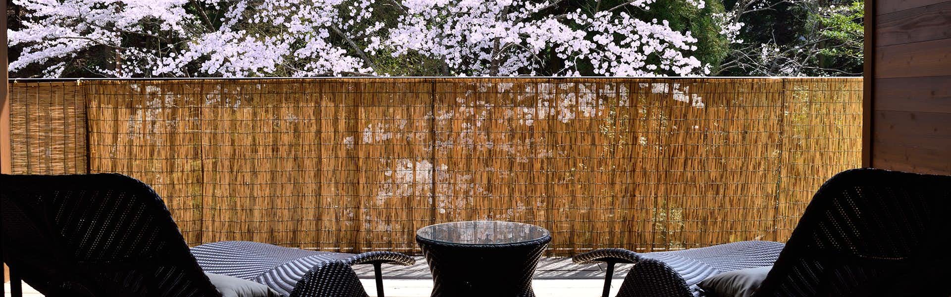 KYO YUNOHANA RESORT Suisen with dark chairs, a round table, bamboo screen, and flowering trees