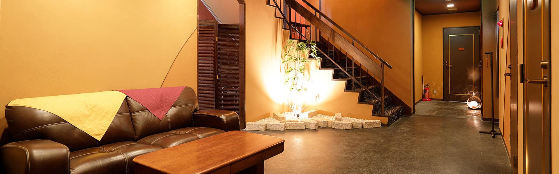 Hidden Hot Spring Inn Tsuki no Akari Lobby sitting area with black leather sofa, wooden table, warm accent lighting, stone planter, and staircase leading upstairs