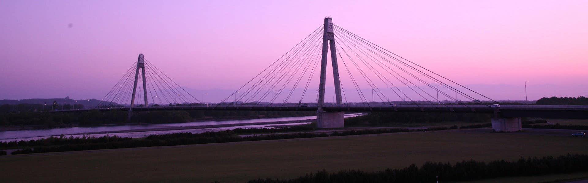 Tokachigawa Onsen Daiichi Hotel with a cable-stayed bridge silhouetted against a purple sunset.