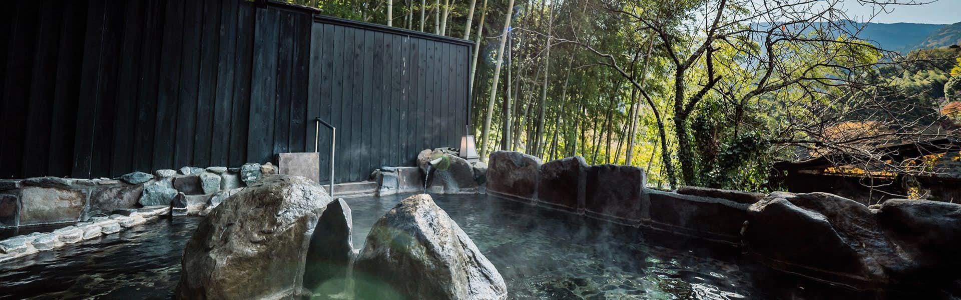 Albergo Yuraku with a rock-lined outdoor bath sheltered by black timber walls.