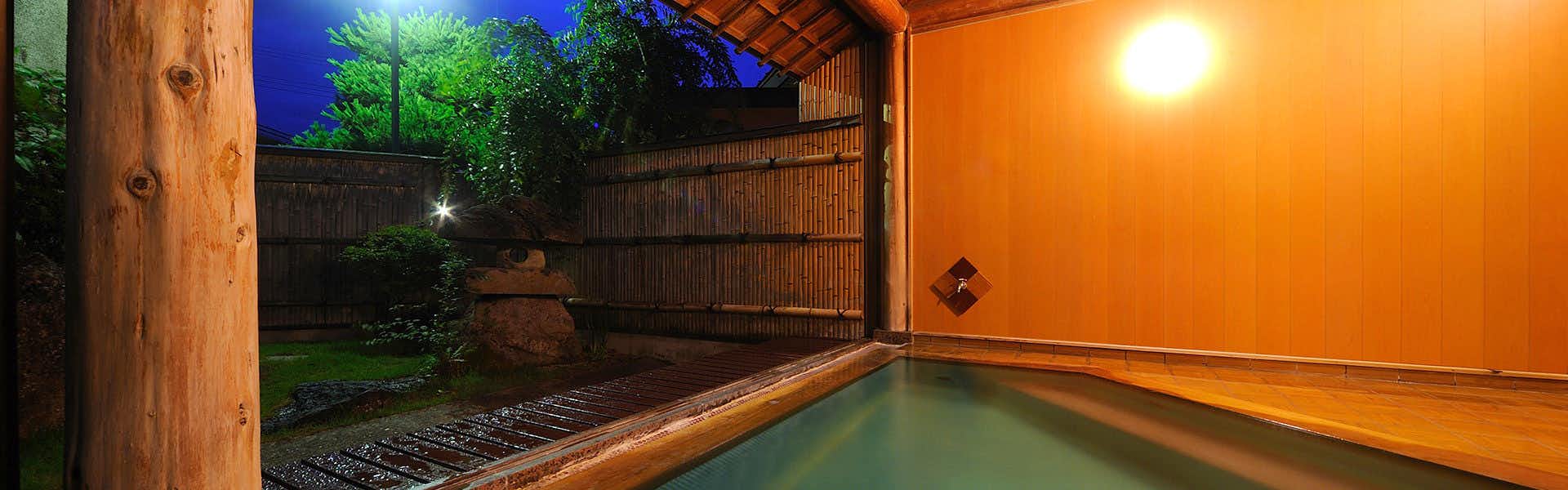 Akayu Onsen Mori no Yu Wooden-edged bath glowing beneath warm wall lights, with timber posts, stone paving, and an open garden side.