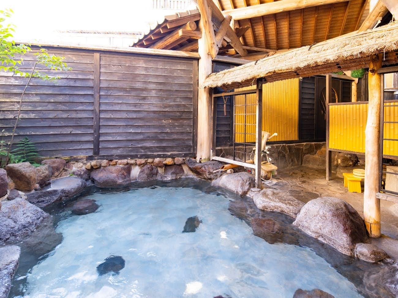Kamioka Onsen Hozanso with this scene, where a second outdoor bath curves around rocks beside timber walls and a tiled roof.