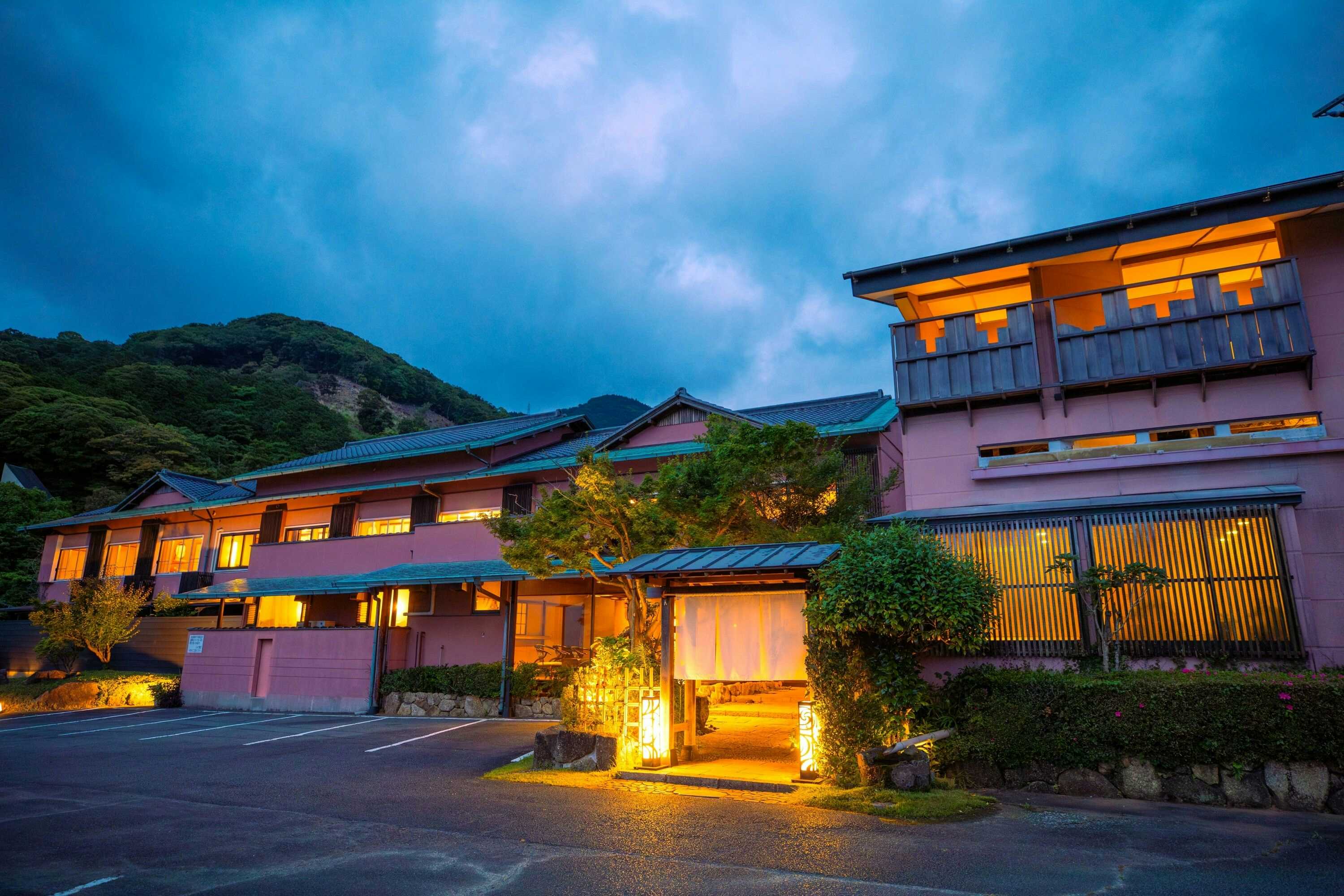 Omoide Nojinde with the illuminated ryokan facade beneath blue evening clouds.