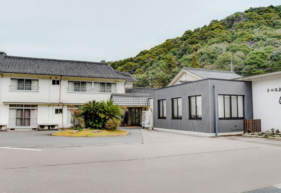 White ryokan buildings around a paved forecourt beneath a wooded hill.