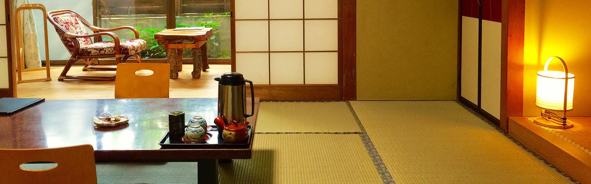 Kamekiyo Ryokan tatami room with a low table, glowing floor lamp and garden chairs.