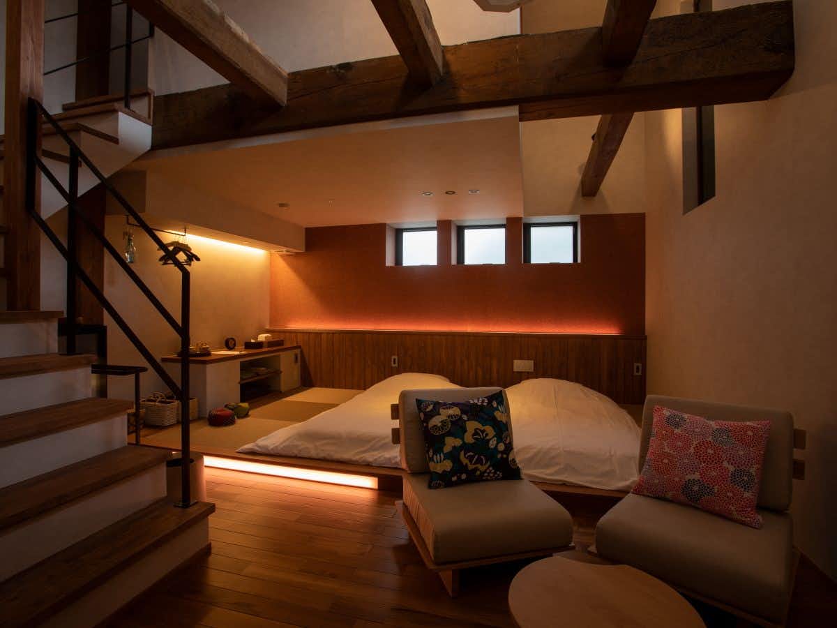 Etchu Inami Machiya Ryokan Kokarian loft-style bedroom with a low bed, chairs and exposed timber beams