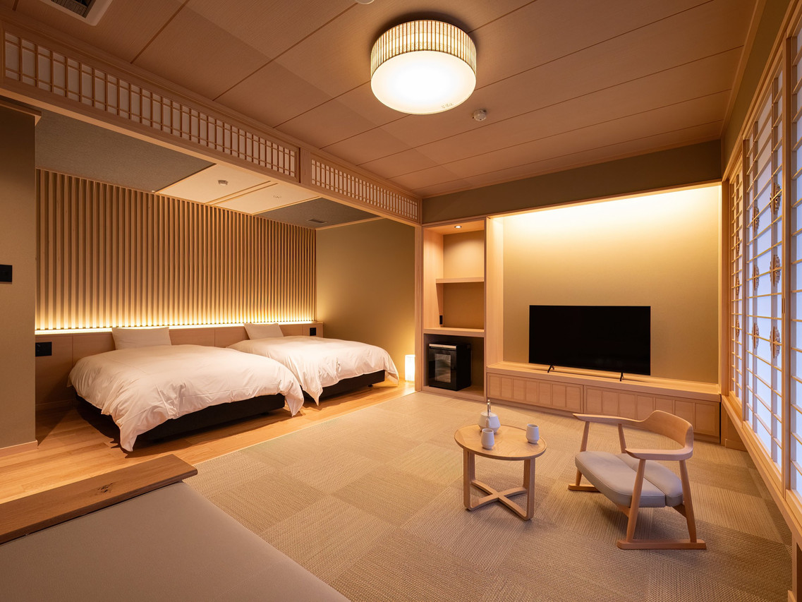 A softly lit room combines low seating with a neatly made bed.