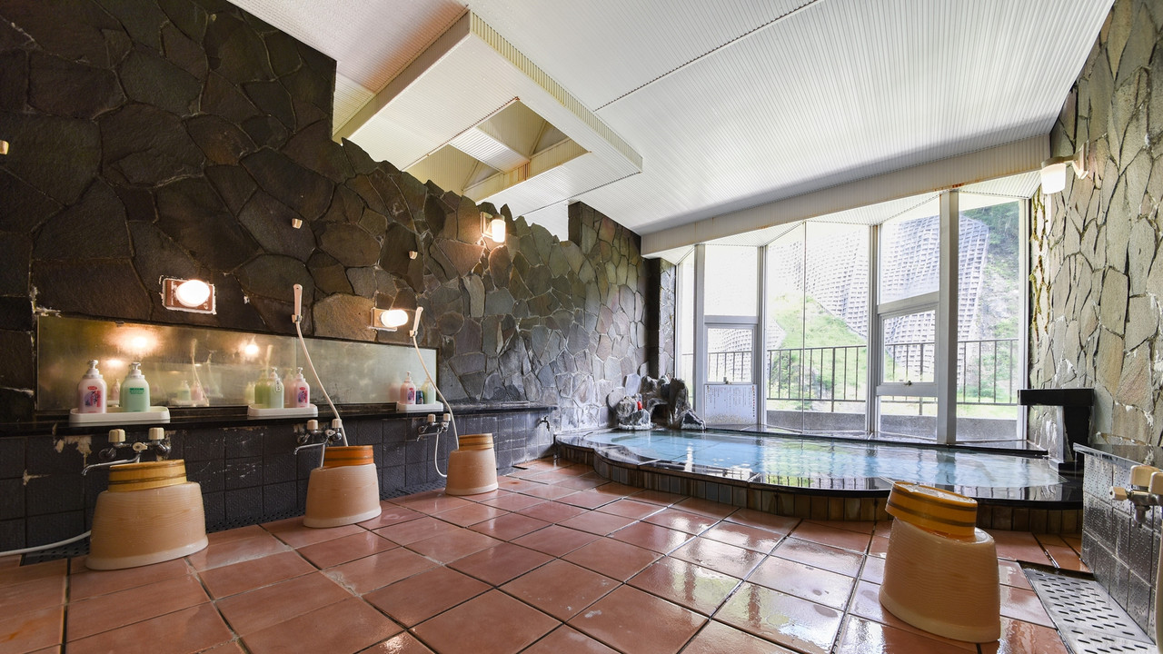 A stone-lined indoor bath is framed by large windows.