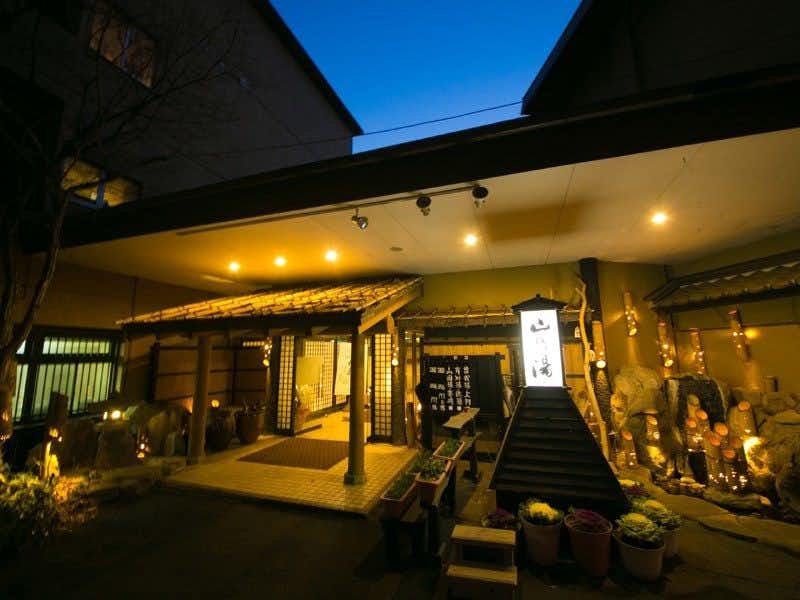 Kinosato Yama no Yu with a warmly lit entrance surrounded by dark garden planting.