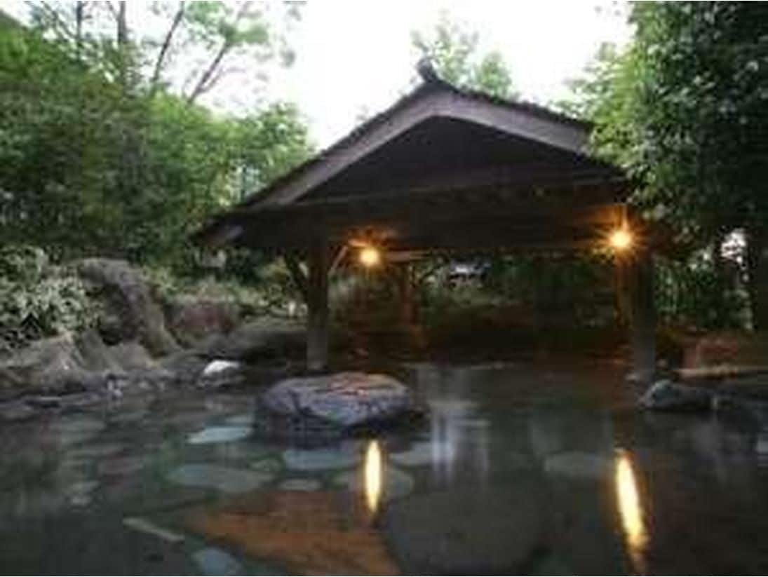 Kurokawa Onsen Yume Ryokan with a rock-lined open-air bath surrounded by forest greenery.