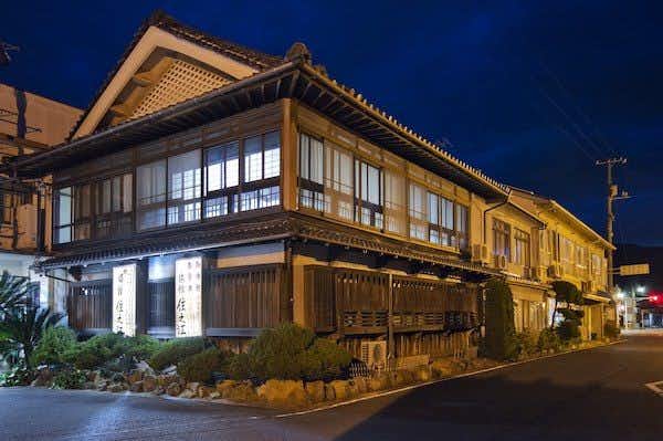 Suminoe Ryokan Multi-story traditional wooden building with latticed windows, illuminated at night, decorative roof with trim, and landscaped surroundings.
