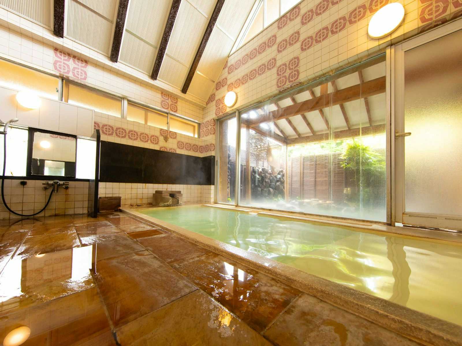 A spacious indoor bath reflecting timber beams and garden light.