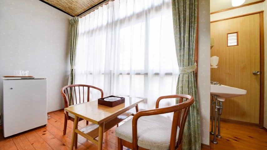 Kawatana Onsen Ryokan Kotengu with this scene, where its window-side wooden chairs stand on polished flooring behind a tatami room.