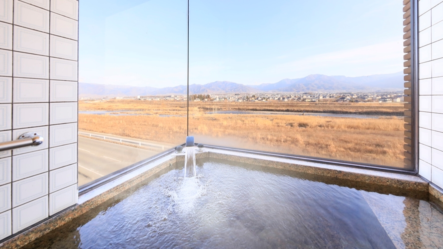 An indoor tiled bath beside large windows overlooking fields and mountains.