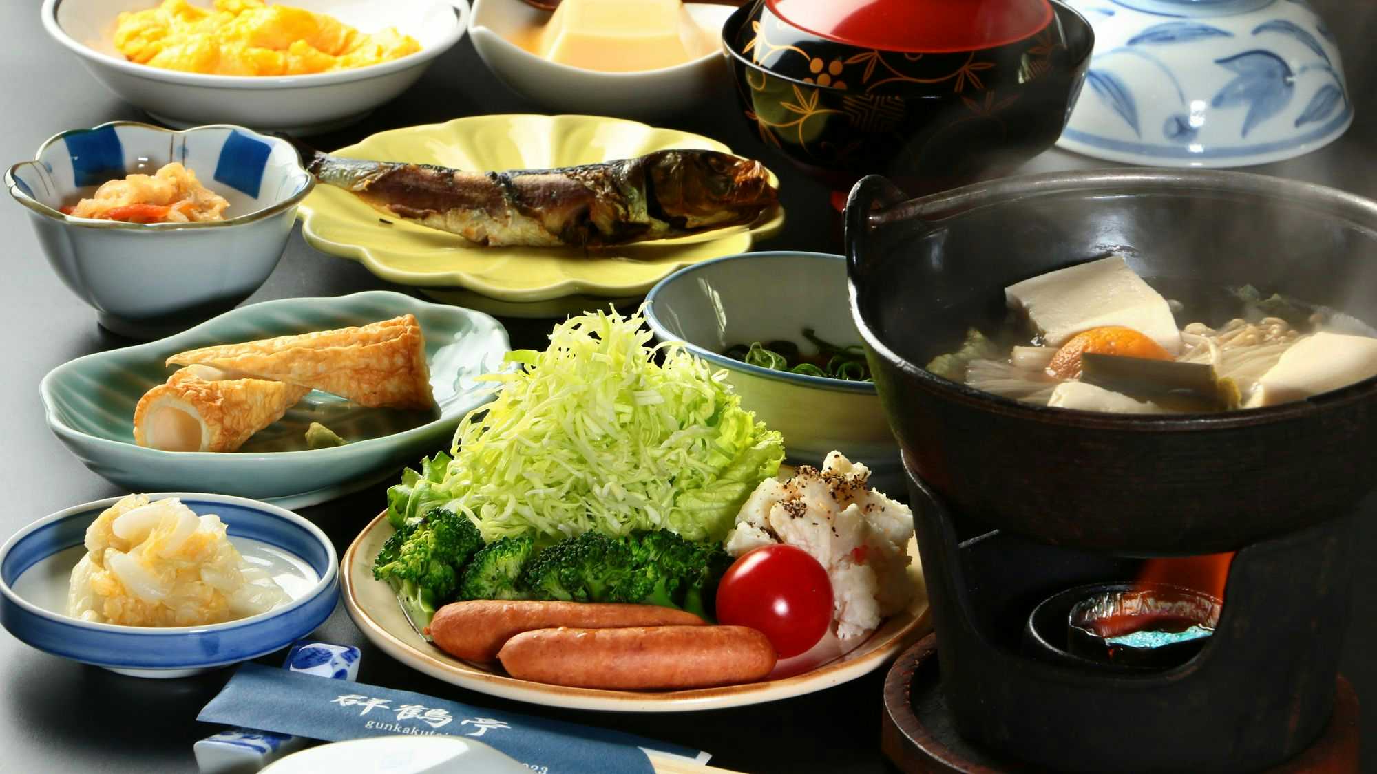 Gunkakutei Multiple white and cream-coloured bowls and platters arranged with prepared items in browns, greens, and reds, accompanied by a dark ceramic vessel.