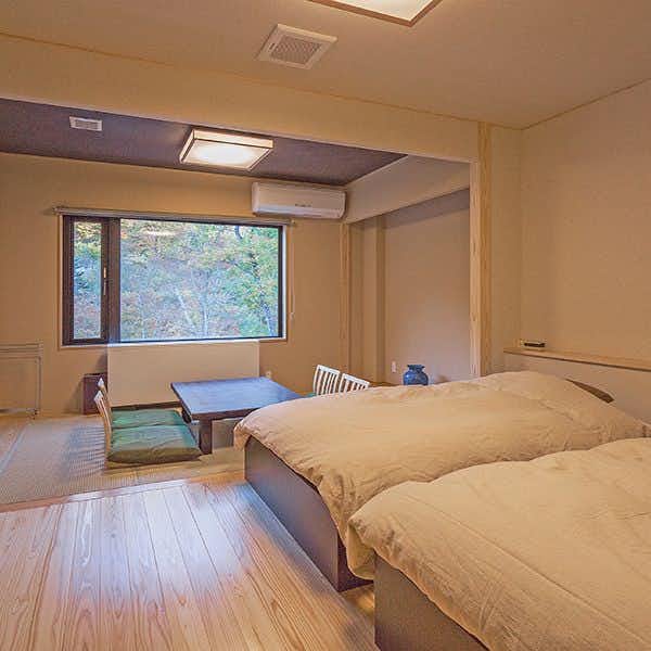 Marukiya Ryokan with a bright twin bedroom with pale timber floor and mountain window.