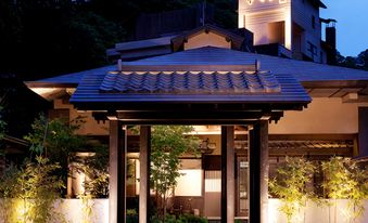 Illuminated traditional entrance canopy framed by bamboo and garden plantings at night.