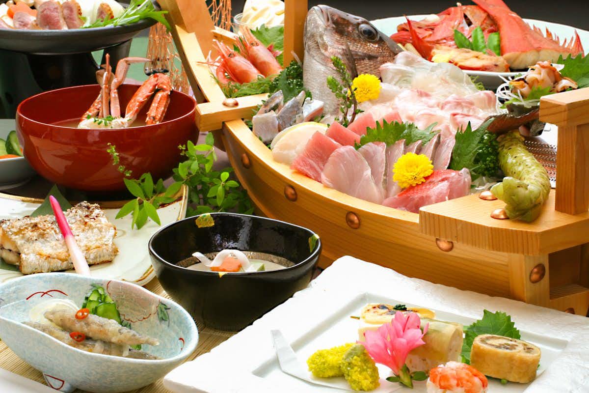 Taste and Hot Spring Inn New Tomiyoshi with a wooden boat platter filled with sashimi and shellfish.