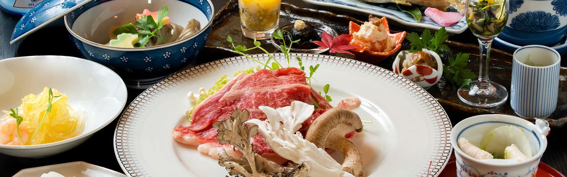 Shiriyaki Onsen Hoshigaoka Sanso White plate with red sliced items, white sliced items, tan mushrooms, green herbs, glass of amber liquid, blue and white cloth.