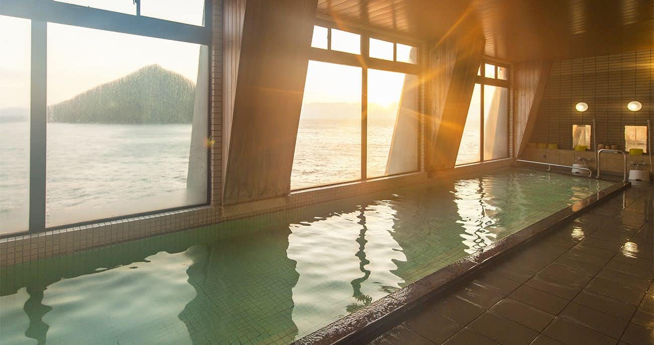 Spectacular View Inn Asamushi Sakura Kanko Hotel with a broad indoor bath facing the sea through tall windows.