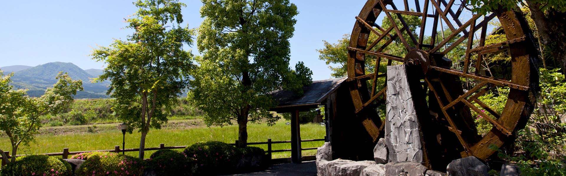 Gokuraku Onsen Takumi no Yado with a wooden waterwheel standing among trees beside the garden.