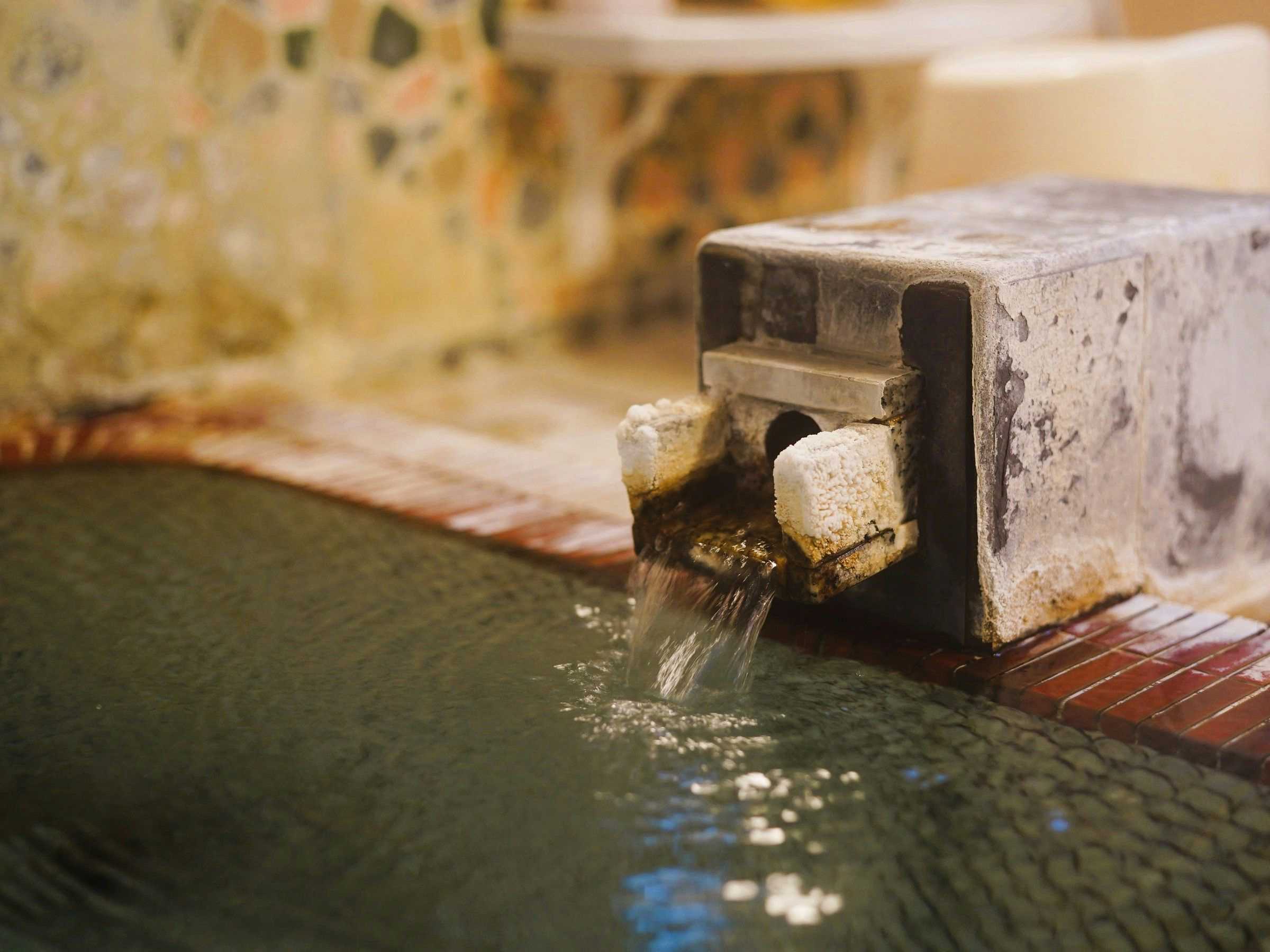 Sakae no Yu Ryokan with a tiled bath filled beside a squared stone spout.