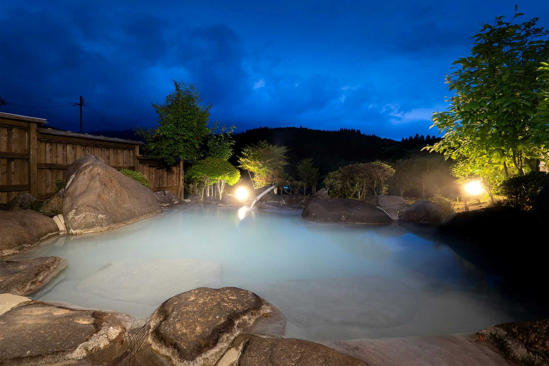Sky Bath Mountain Lodge Hanayu with a steaming outdoor rock bath under a deep blue evening sky.