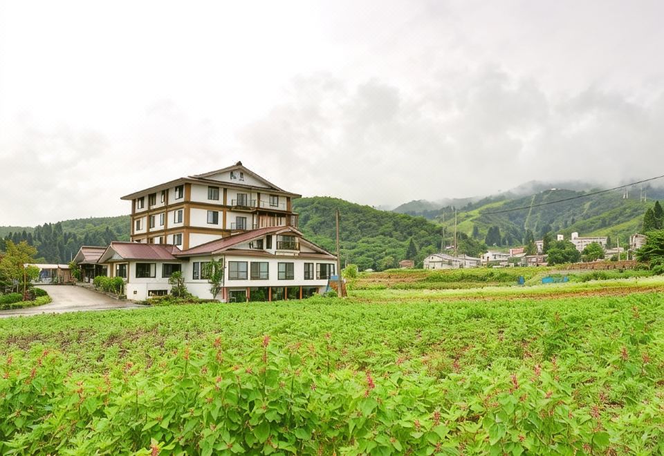 A hotel building beside green fields and mountains.