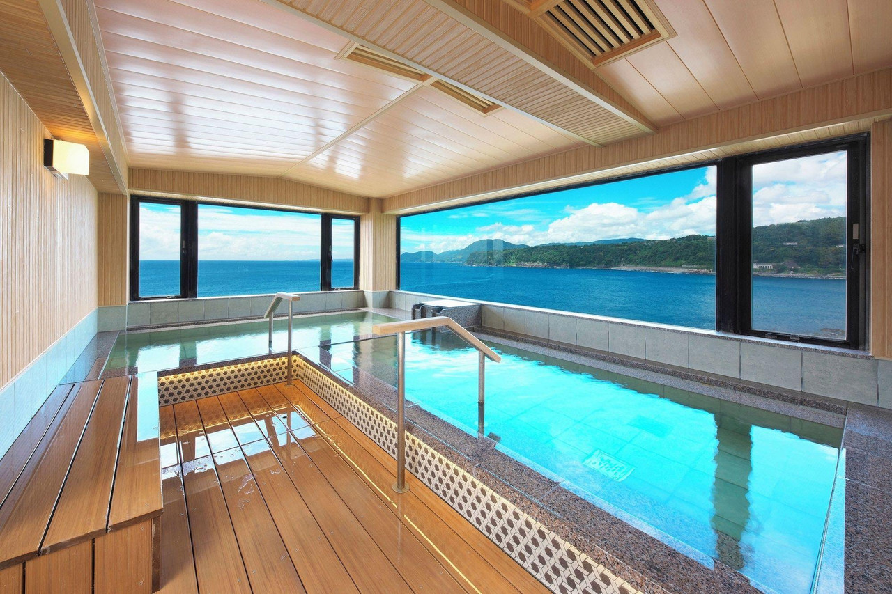 A bright indoor bathing pool spans a wood-paneled room with wide windows over the blue sea.