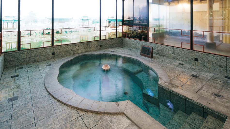 Gyokusenkaku with a rounded indoor bath beneath panoramic city windows.