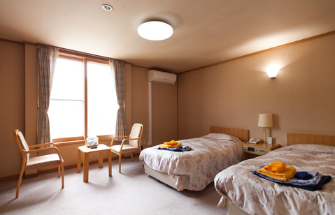 Western-style guest room with twin beds, chairs and a round table by the windows.