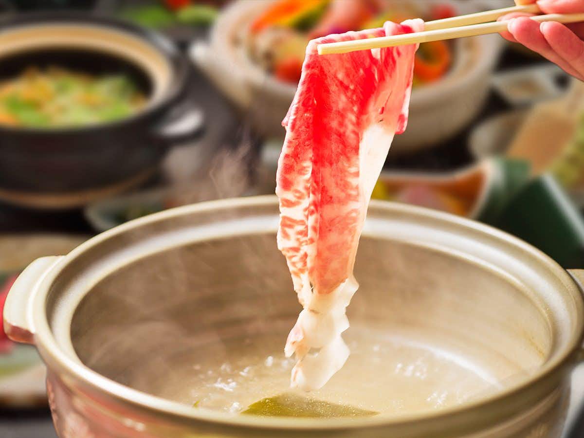 Yumoto Sakakibara-kan with thin beef slices held above a simmering hot pot.