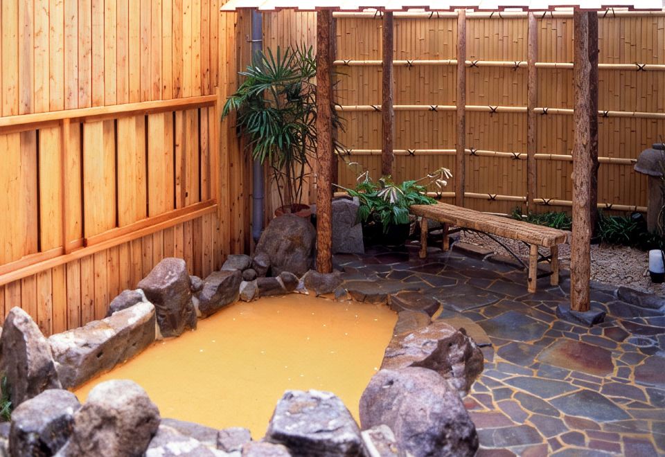 A rock-lined outdoor bath beside bamboo screens.