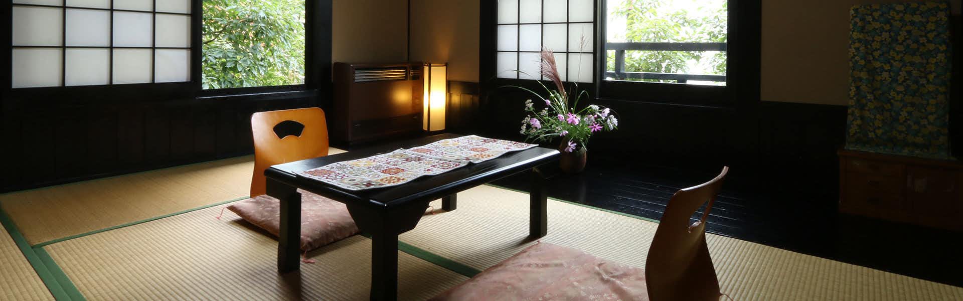 Shukubo Hanashinobu Dark wooden low table with patterned surface, illuminated fixtures above with warm metallic tones, gridded window structure, orchid arrangement, and wooden seating