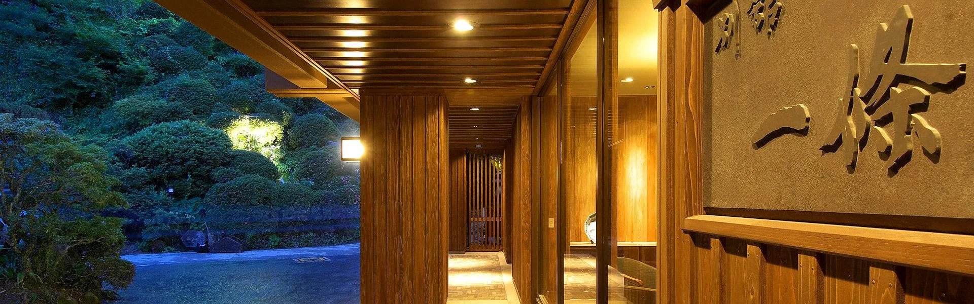 Yumushi Ichijo's illuminated entrance corridor at night, forested hillside of Shiroishi behind