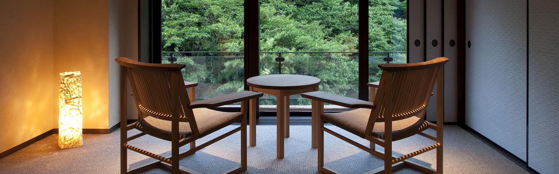 Shima Onsen Yamaguchikan with two wooden chairs and a round table facing large green windows