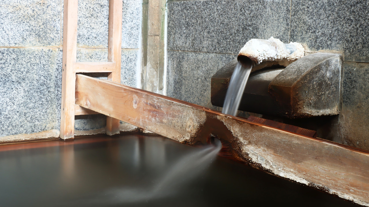 A wooden spout flowing into a stone-lined bath.
