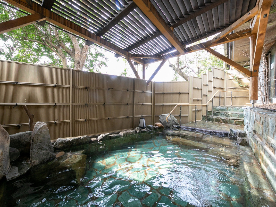 A broad outdoor pool sits beneath a slatted roof.