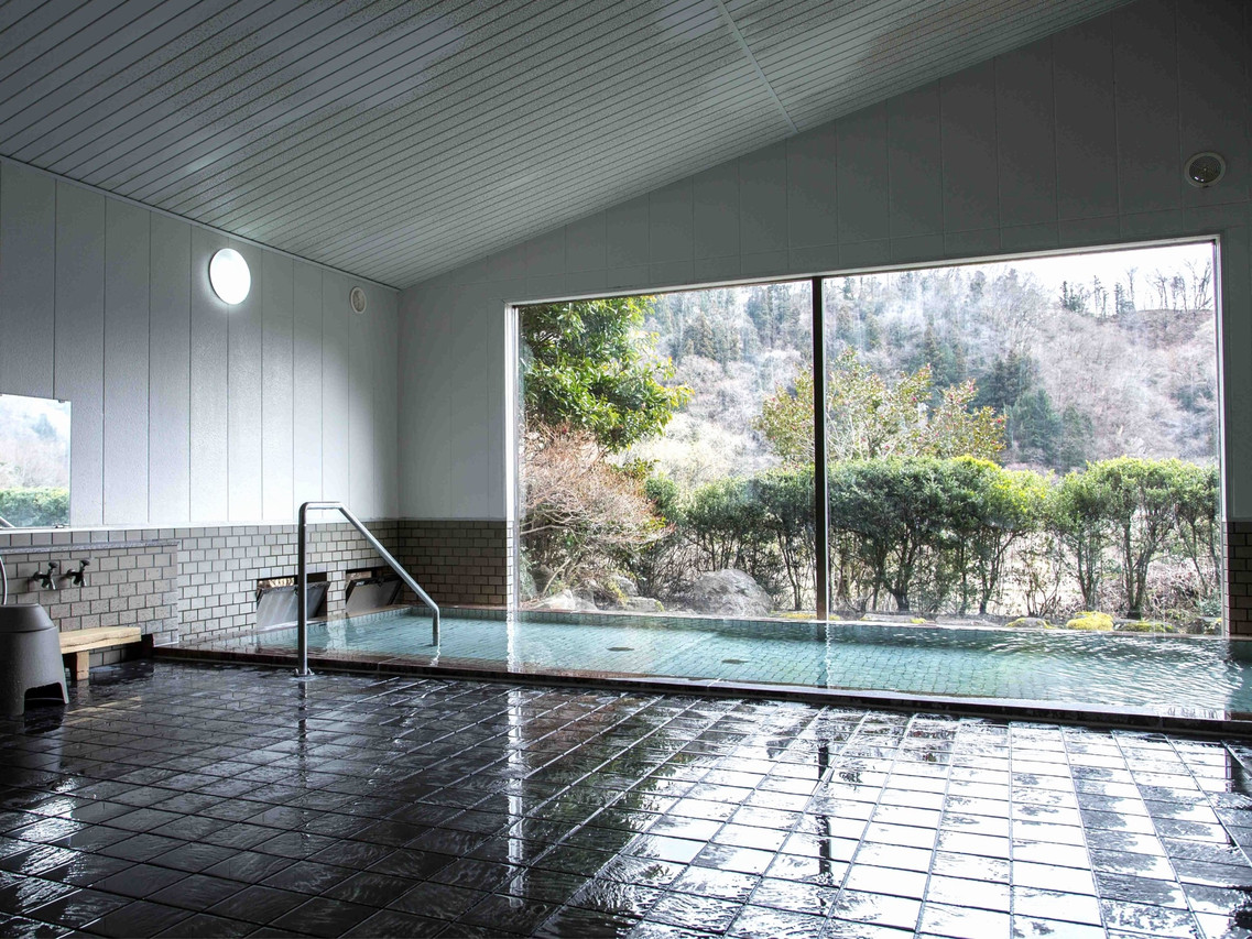 A tiled bathing room has a broad window facing the trees.