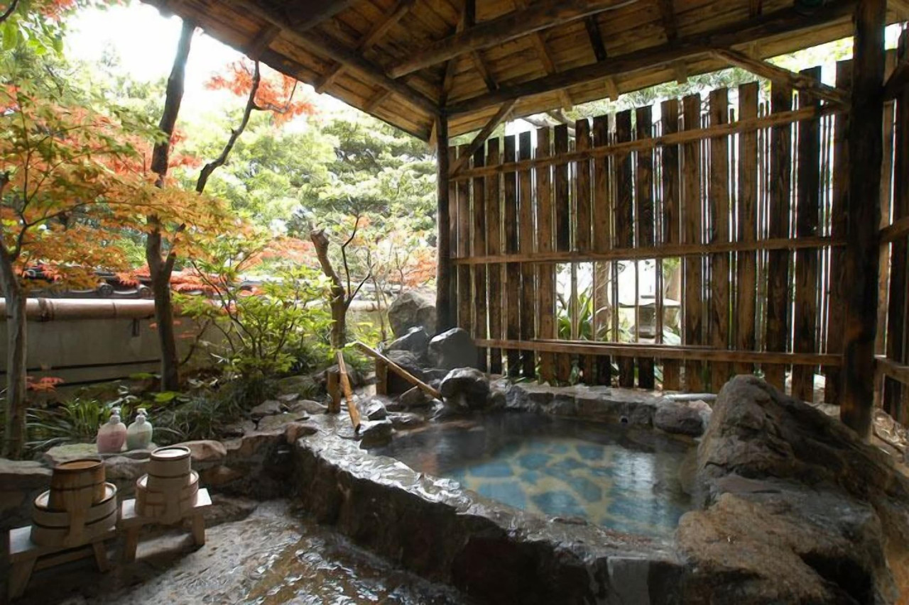 A roofed outdoor rock bath surrounded by trees.