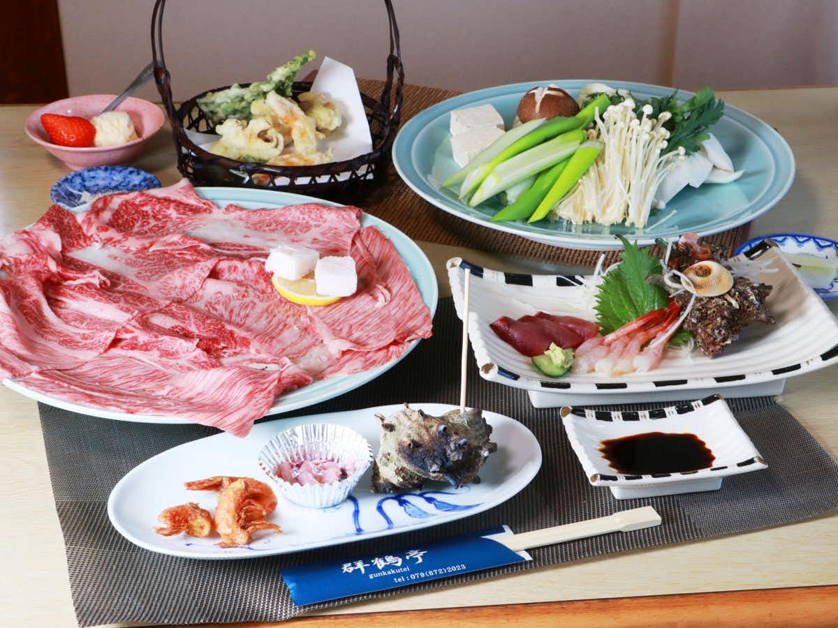 Gunkakutei Multiple white and blue plated items arranged with red and pink slices, green strips, white garnish, and dark accents on striped mat.