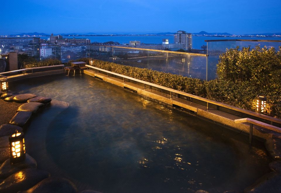 A rooftop bath overlooking a city at dusk.