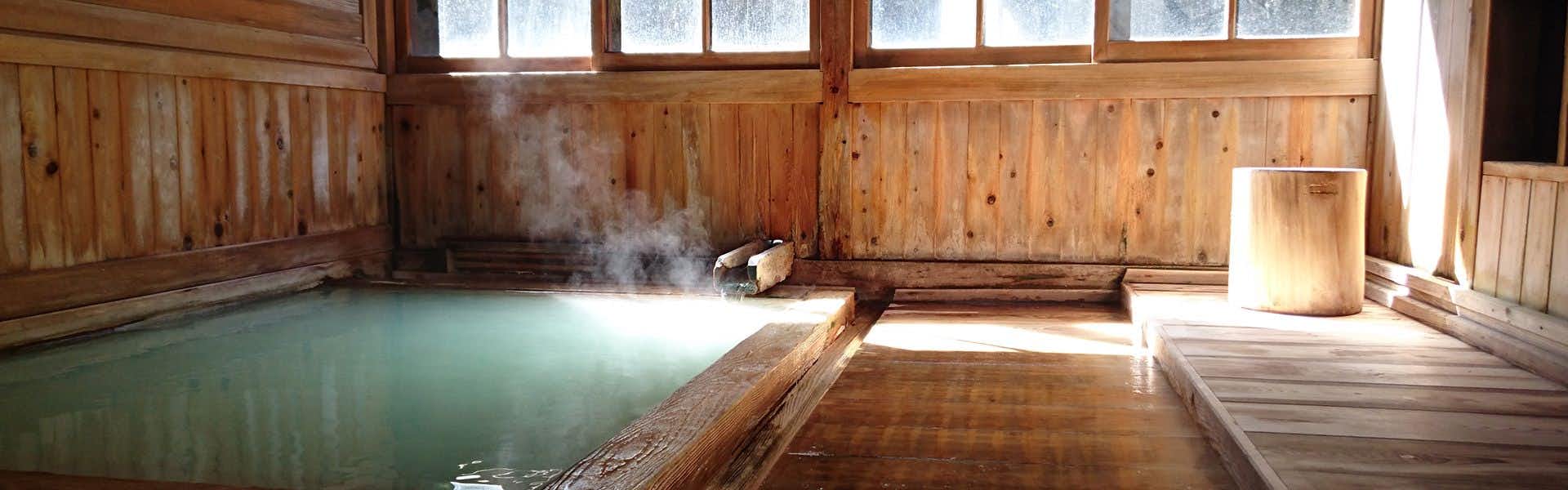 Ryokan Tamagoyu with a timber-lined indoor bath filled with pale mineral water.