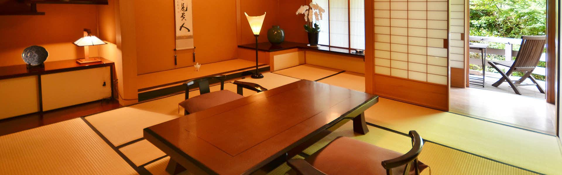 Kaiseki Inn Ogiya Traditional tatami room with low wooden table, black cushions, shoji screens, and warm lighting from lanterns and windows.