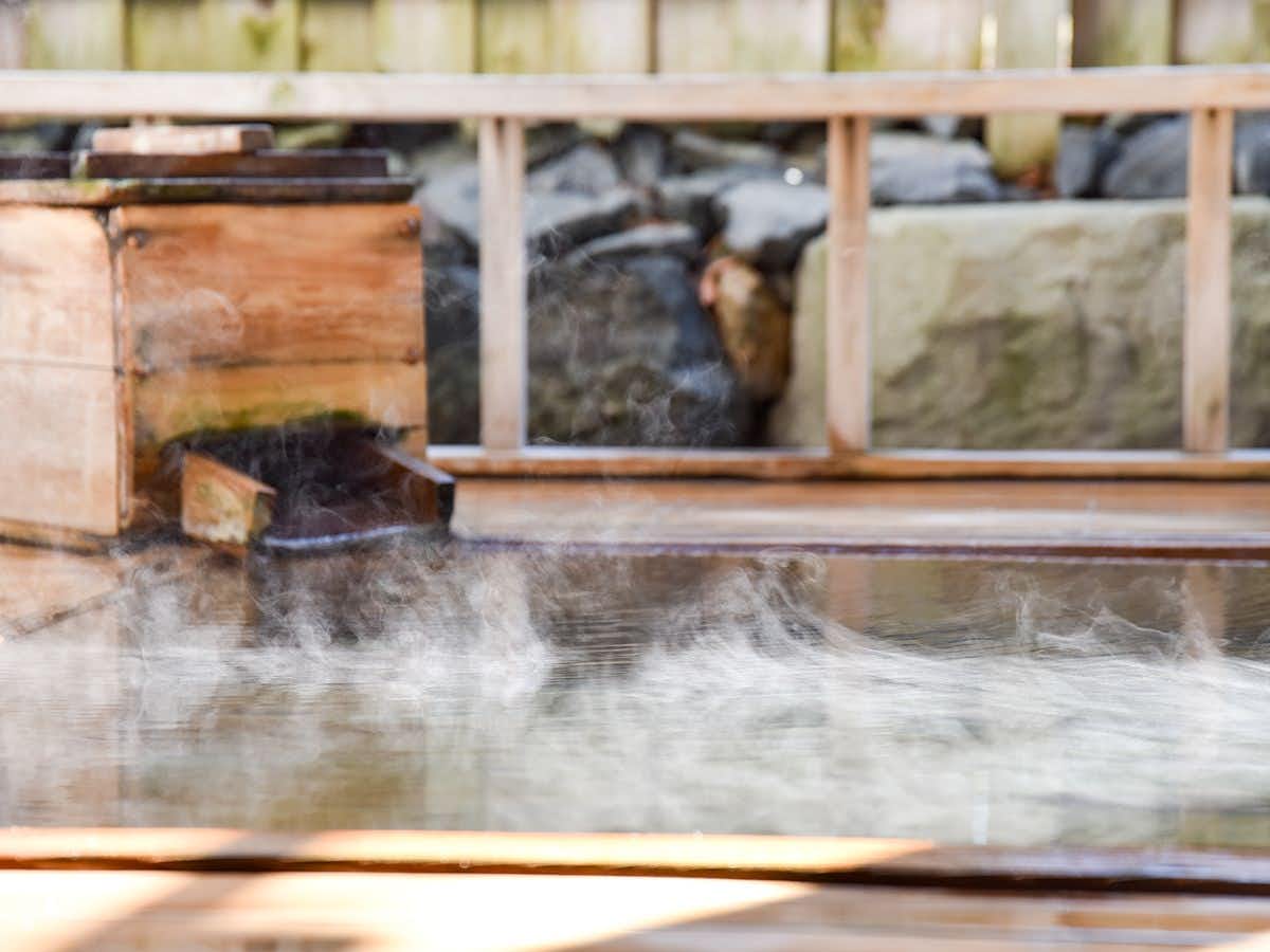 Tsugaru Clan Honjin Inn Yanagi no Yu with a steaming outdoor bath beside a timber railing.