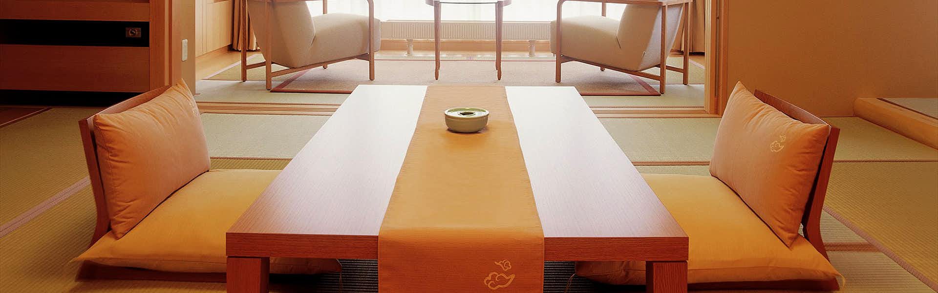 Kusatsu Onsen Bouun Tatami sitting room with low wooden table, two orange floor cushions, and window seating with armchairs
