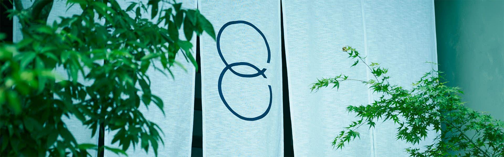 Tsuki to Maguro Ishigami a white noren curtain with a circular emblem framed by foliage.