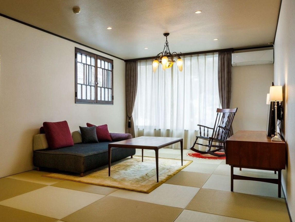 Tatami room with a sofa, low table, rocking chair, curtained window, and wood cabinet.