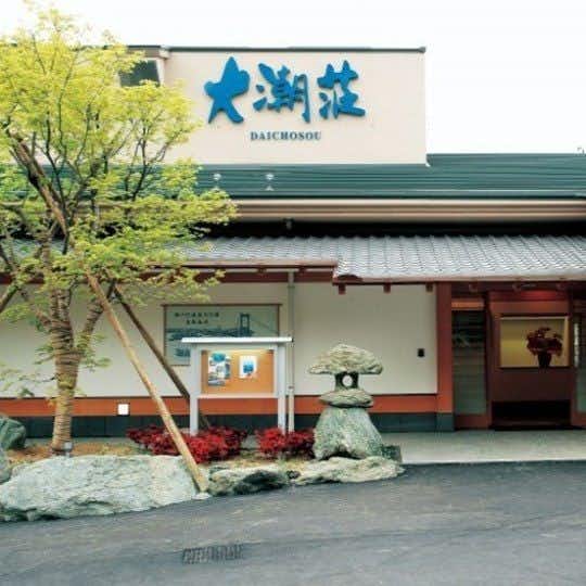 Daichoso white lodging entrance with a large blue sign, trees and stone lantern